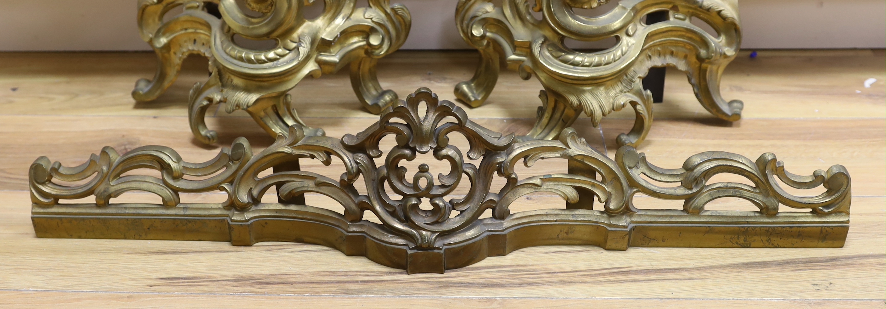 A French rococo revival gilt bronze fender with scroll work and bar, largest 44cm high